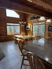 Dining space featuring a wood ceiling with exposed beams, plenty of natural light, light tile patterned floors, suspended lighting, and log walls