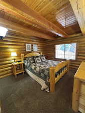 Bedroom with a wood ceiling with exposed beams, rustic walls, and carpet flooring