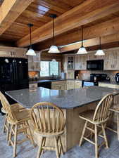Kitchen with a wooden ceiling with exposed beams, a kitchen bar, black appliances, and decorative light fixtures
