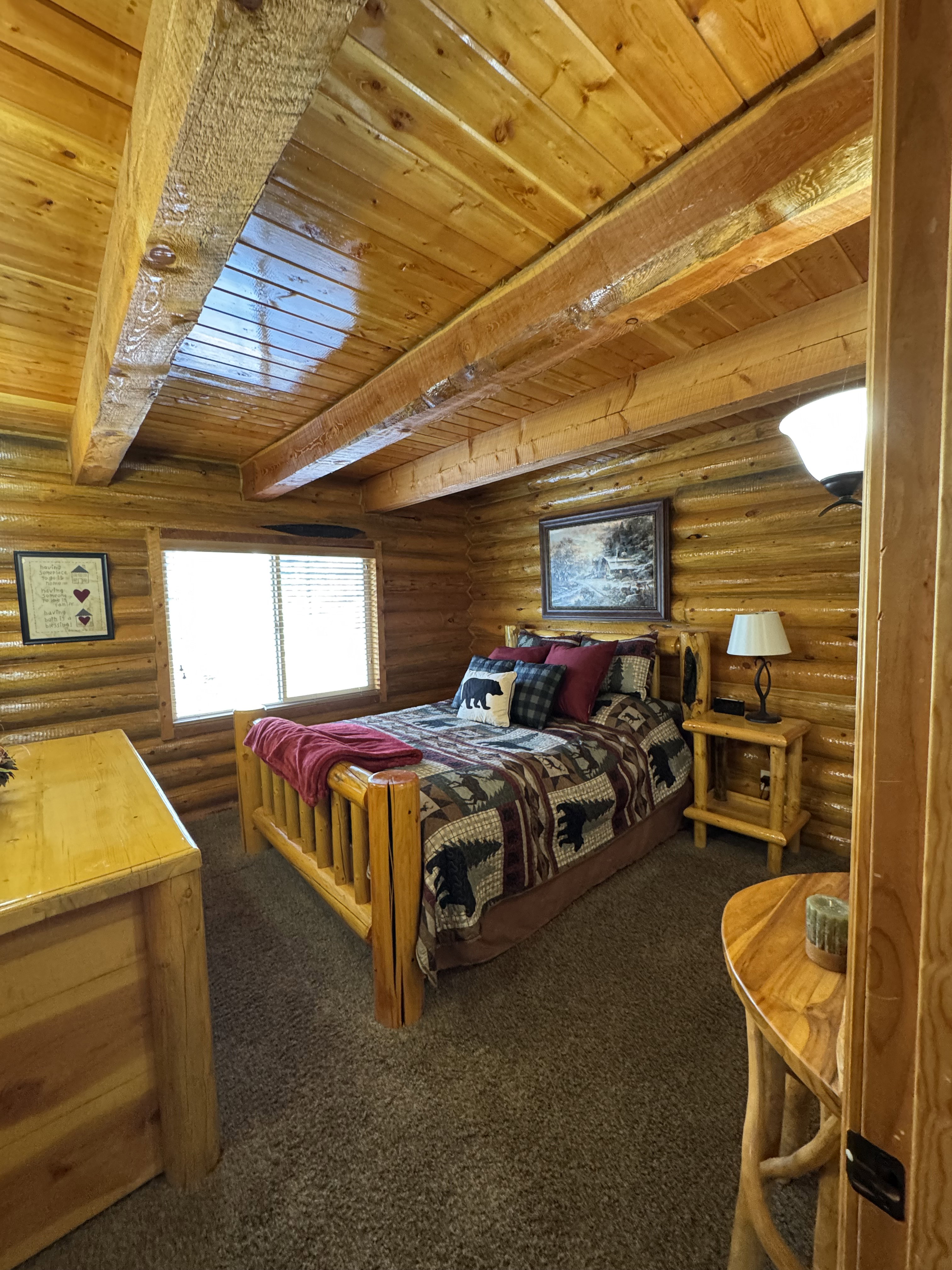 Bedroom with a wood ceiling with exposed beams, log walls, and dark colored carpet