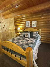 Bedroom featuring carpet, rustic walls, and a wood ceiling with exposed beams