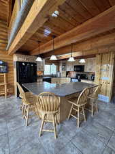 Kitchen featuring a wooden ceiling with exposed beams, black appliances, a spacious island, decorative light fixtures, and dark granite  countertops