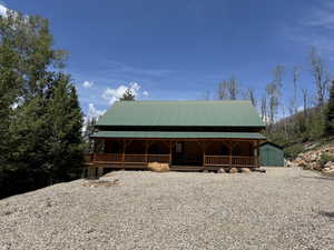 Log cabin exterior featuring a green metal roof, a full-width covered porch with wood railings, and a gravel driveway
