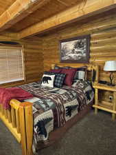 Bedroom with dark colored carpet, log walls, and a wooden ceiling with exposed beams