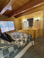 Bedroom featuring rustic walls, carpet floors, and a wooden ceiling with exposed beams