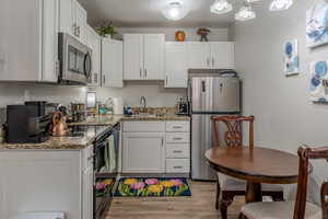 Kitchen featuring stainless steel appliances, white cabinetry, a textured wall, light stone countertops, and light wood finished floors