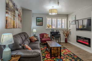 Living area featuring wood finished floors, a textured ceiling, and a glass covered fireplace