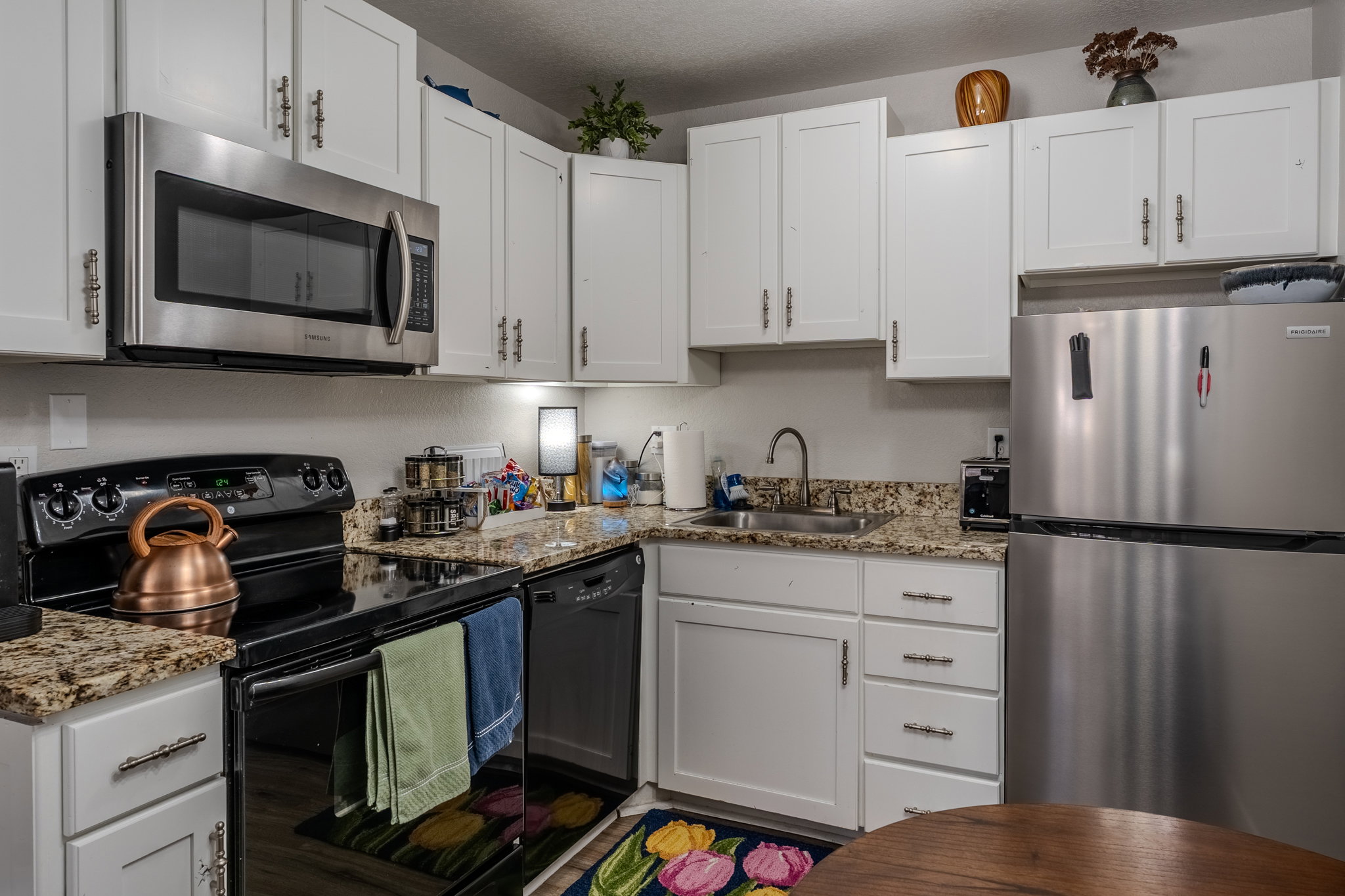 Kitchen with black appliances, white cabinets, light stone countertops, and a textured ceiling