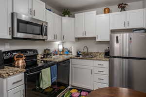 Kitchen with black appliances, white cabinets, light stone countertops, and a textured ceiling
