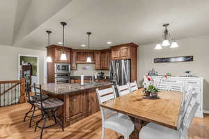 Kitchen with wood finish cabinetry, a kitchen bar, dark stone counters, light wood finished floors, and a kitchen island with sink