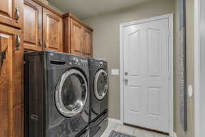 Laundry area with cabinet space, light tile patterned floors, and separate washer and dryer