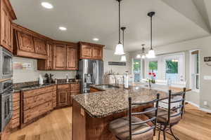 Kitchen featuring dark stone counters, light wood-style flooring, stainless steel appliances, wood finish cabinets, and a kitchen bar