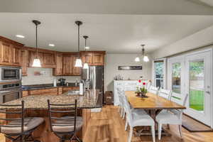 Kitchen with a center island with sink, wood finish cabinets, dark stone countertops, stainless steel appliances, and a chandelier