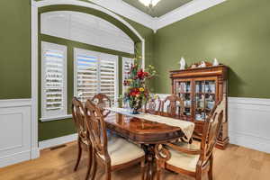 Dining room featuring a wainscoted wall, a decorative wall, ornamental molding, and wood finished floors