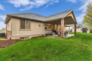 Rear view of property featuring a patio area, a yard, a storage unit, roof with shingles, and stucco siding