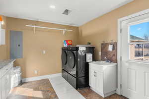 Laundry area featuring electric panel, cabinet space, stone tile flooring, and washer and dryer