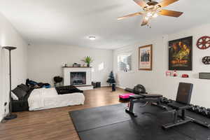 Workout area featuring wood finished floors, a brick fireplace, a textured ceiling, and ceiling fan