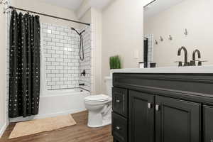 Full bathroom featuring vanity, shower / bath combo with shower curtain, and dark wood-type flooring