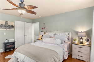 Bedroom featuring wood finished floors, a wood stove, and ceiling fan