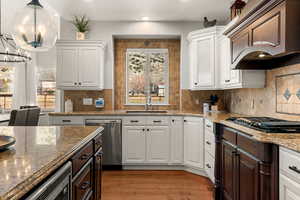 Kitchen with dual tone cabinets, dark stone countertops, light wood-type flooring, stainless steel appliances, and a chandelier
