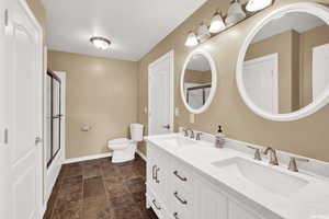 Full bathroom with double vanity, dark stone finish flooring, and bath / shower combo with glass door