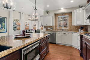 Kitchen featuring two tone color scheme, stainless steel appliances, light stone counters, light wood-type flooring, and backsplash