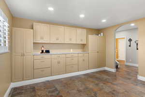 Kitchen with arched walkways, light countertops, recessed lighting, dark stone finish flooring, and cream cabinetry