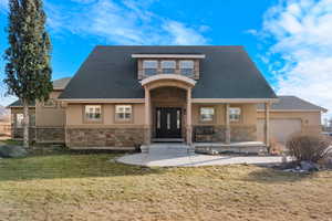 View of front of property with stone siding, a front yard, stucco siding, covered porch, and roof with shingles