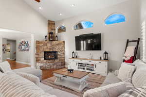 Living area with wood finished floors, a ceiling fan, vaulted ceiling, a fireplace, and arched walkways