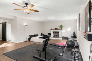 Workout area featuring wood finished floors, a barn door, a ceiling fan, a fireplace with raised hearth, and a textured ceiling