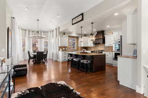 Kitchen with an island with sink, light stone countertops, dark wood-type flooring, a breakfast bar, and two tone cabinets