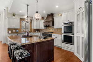 Two tone kitchen with stainless steel appliances, light stone counters, an island with sink, a breakfast bar, and tasteful backsplash
