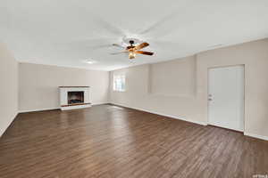 Unfurnished living room featuring a brick fireplace, a ceiling fan, and dark wood-style flooring