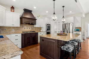 Kitchen with tasteful backsplash, a center island with sink, stainless steel appliances, dark wood finished floors, and dual tone cabinets