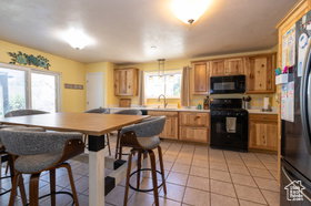 Kitchen featuring black appliances, light countertops, light tile patterned floors, and decorative light fixtures