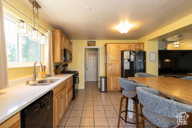 Kitchen featuring black appliances, butcher block counters, light tile patterned floors, light wood finish cabinets, and a kitchen bar