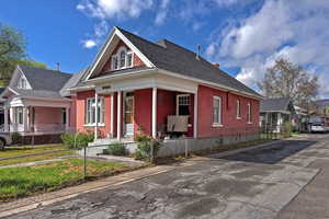View of front of property featuring covered porch, brick siding, roof with shingles, a chimney, and a fenced front yard