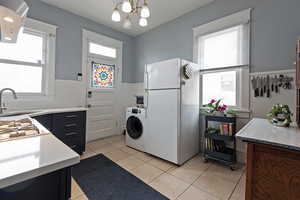 Kitchen with white appliances, island exhaust hood, washer / dryer, light tile patterned floors, and hanging lights