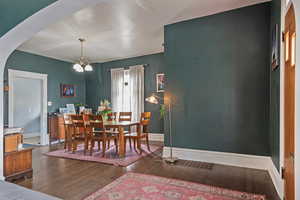 Dining room with dark wood-type flooring, suspended lighting, and arched walkways