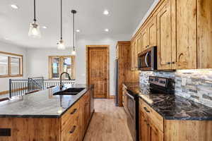 Kitchen featuring stainless steel appliances, a center island with sink, light wood-type flooring, tasteful backsplash, and decorative light fixtures
