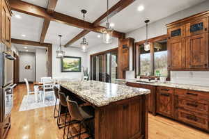 Kitchen with light stone counters, a kitchen island, a breakfast bar area, decorative backsplash, and glass fronted cabinets