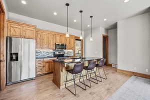 Kitchen with stainless steel appliances, dark stone counters, a kitchen breakfast bar, pendant lighting, and a kitchen island with sink