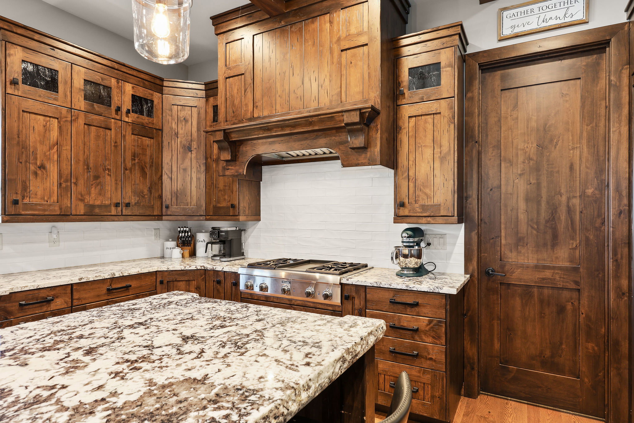 Kitchen featuring glass fronted cabinets, light stone countertops, stainless steel gas cooktop, backsplash, and light wood finished floors