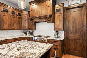 Kitchen featuring glass fronted cabinets, light stone countertops, stainless steel gas cooktop, backsplash, and light wood finished floors