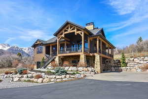 Chalet / cabin featuring stone siding, a chimney, a porch, concrete driveway, and a mountain view