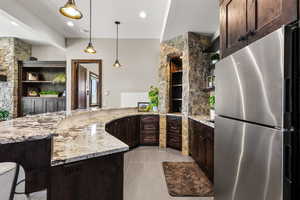 Kitchen featuring open shelves, freestanding refrigerator, dark wood finish cabinets, and light stone countertops