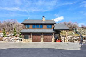View of front facade with roof with shingles, a garage, a chimney, concrete driveway, and stone siding