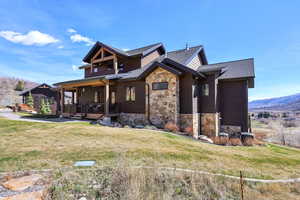 View of property exterior featuring stone siding, a lawn, covered porch, a shingled roof, and a mountain view