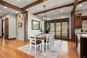 Dining room with light wood-type flooring, suspended lighting, beam ceiling, and french doors