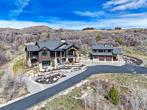 Rear view of house featuring a chimney, stone siding, a mountain view, asphalt driveway, and a patio area